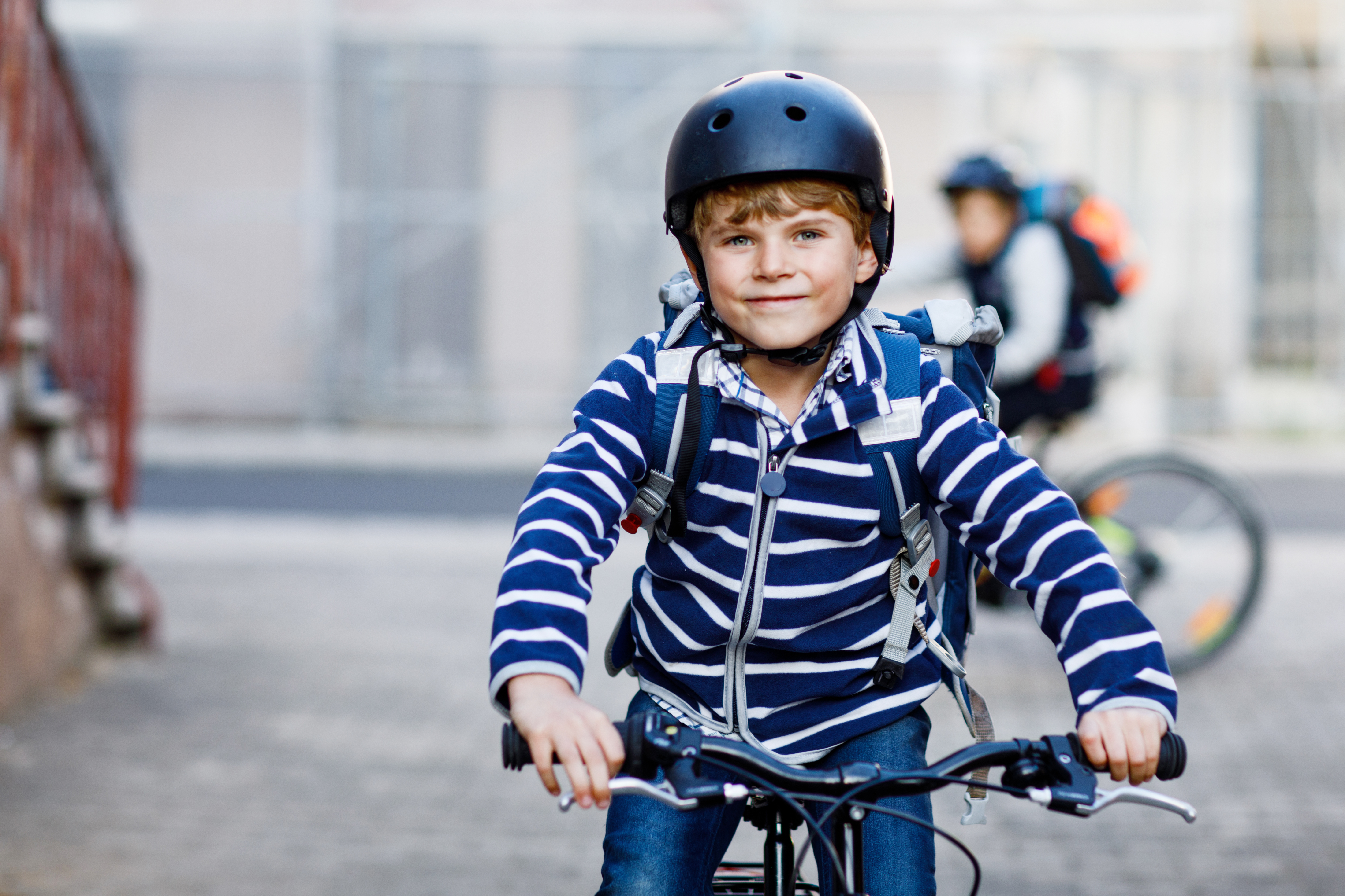 Pojke cyklar med cykelhjälm, någon cyklar bakom honom med hjälm