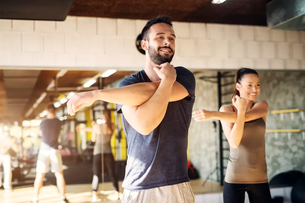 Två personer står och stretchar på gymmet